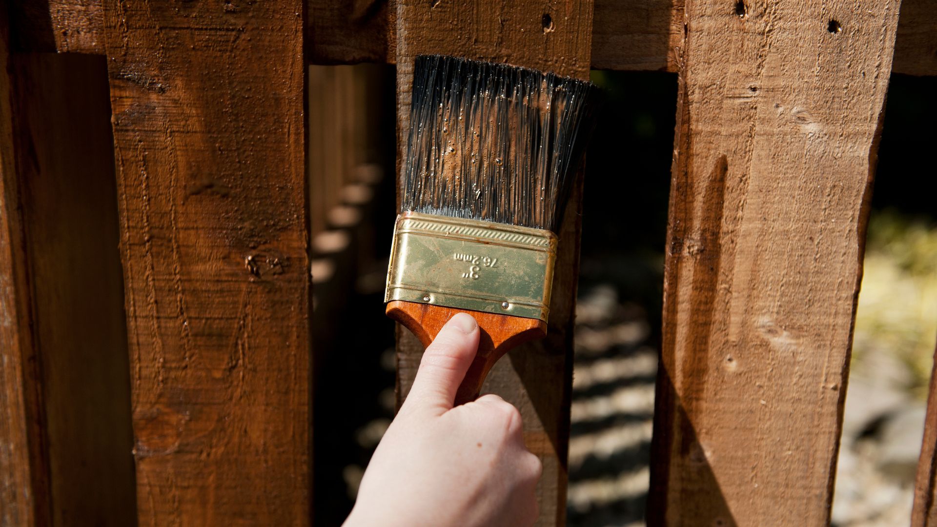 A hand holding a paint brush over a wooden fence