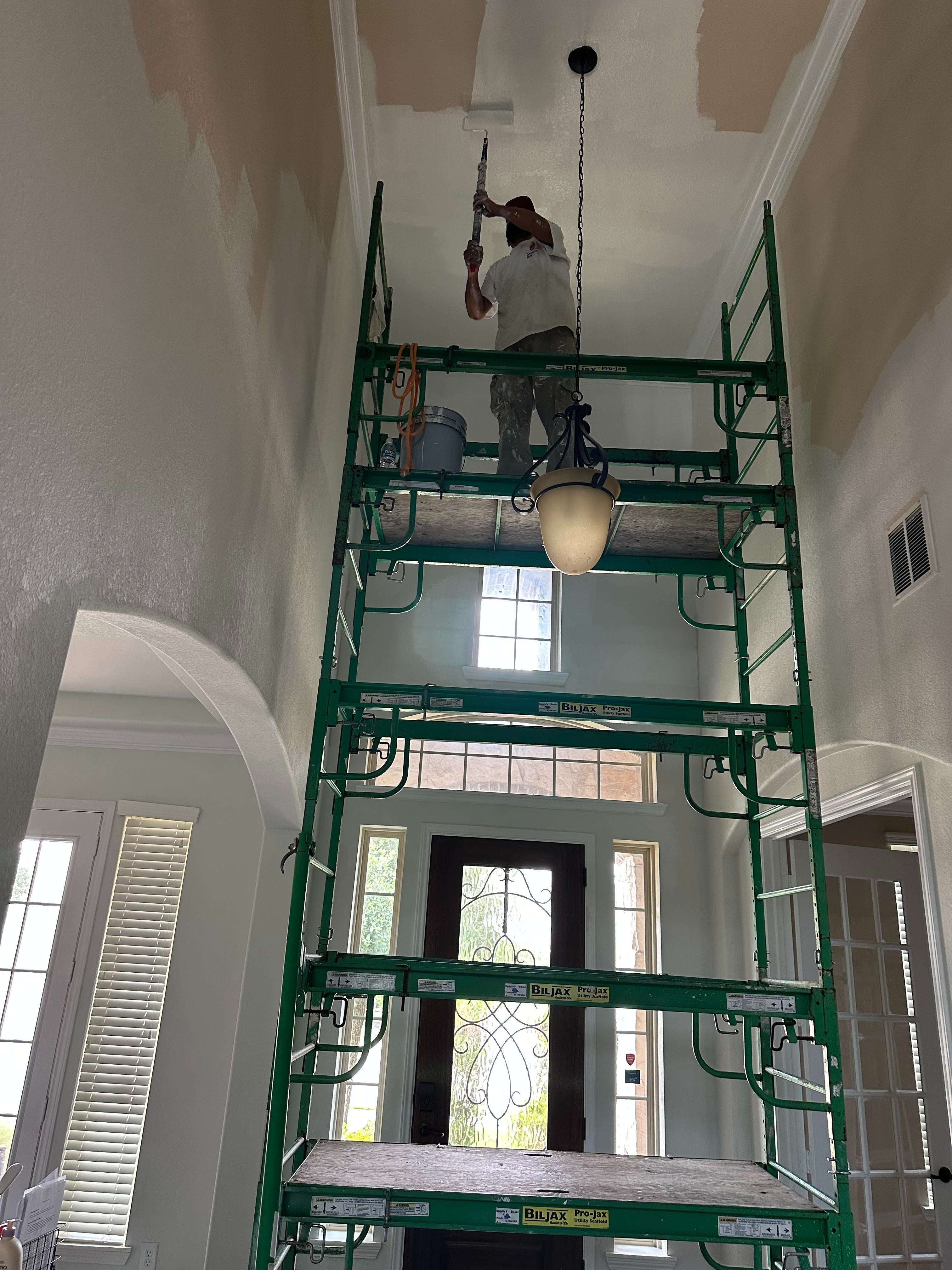 A man on a green ladder painting the ceiling