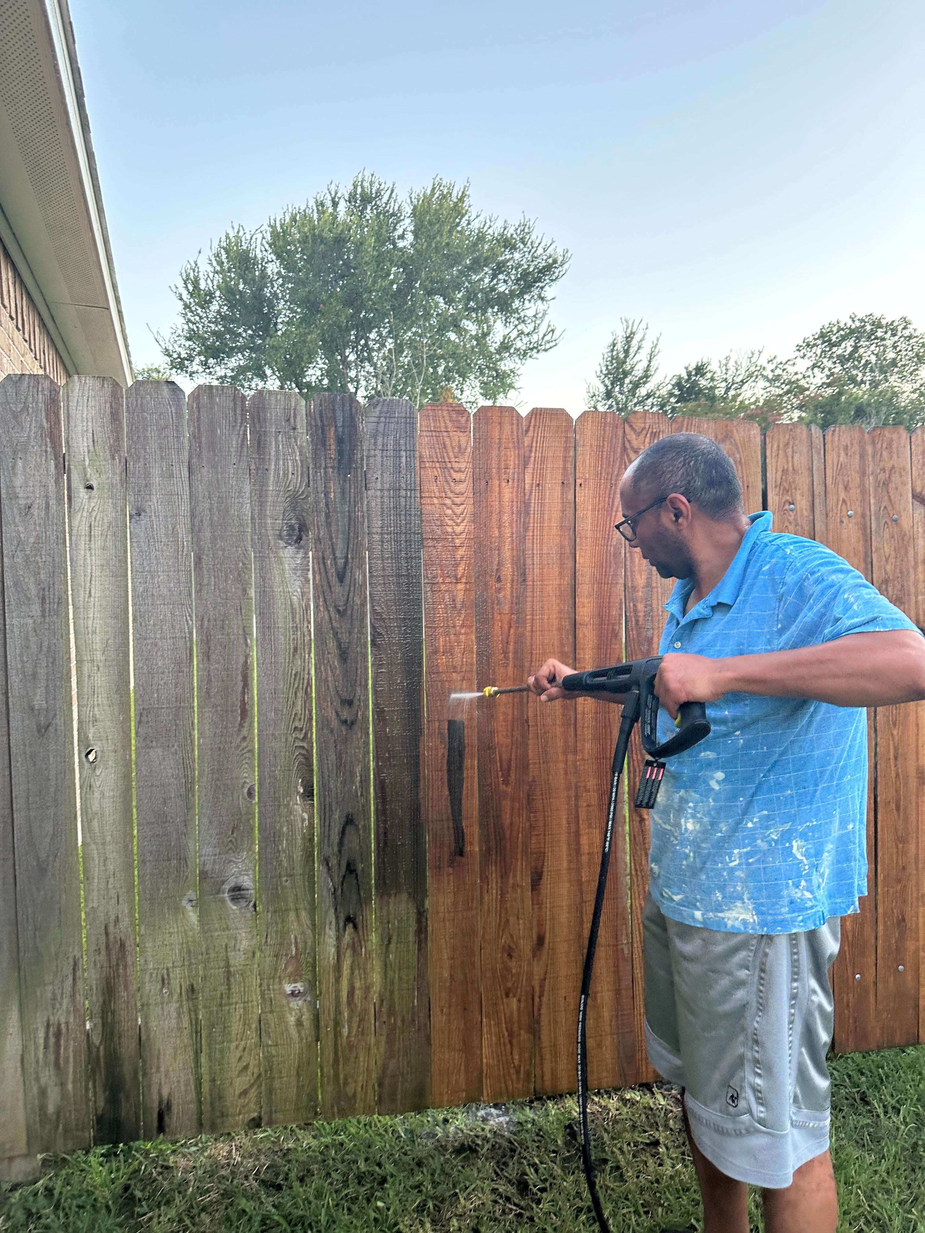 A man using a pressure washer to clean a fence