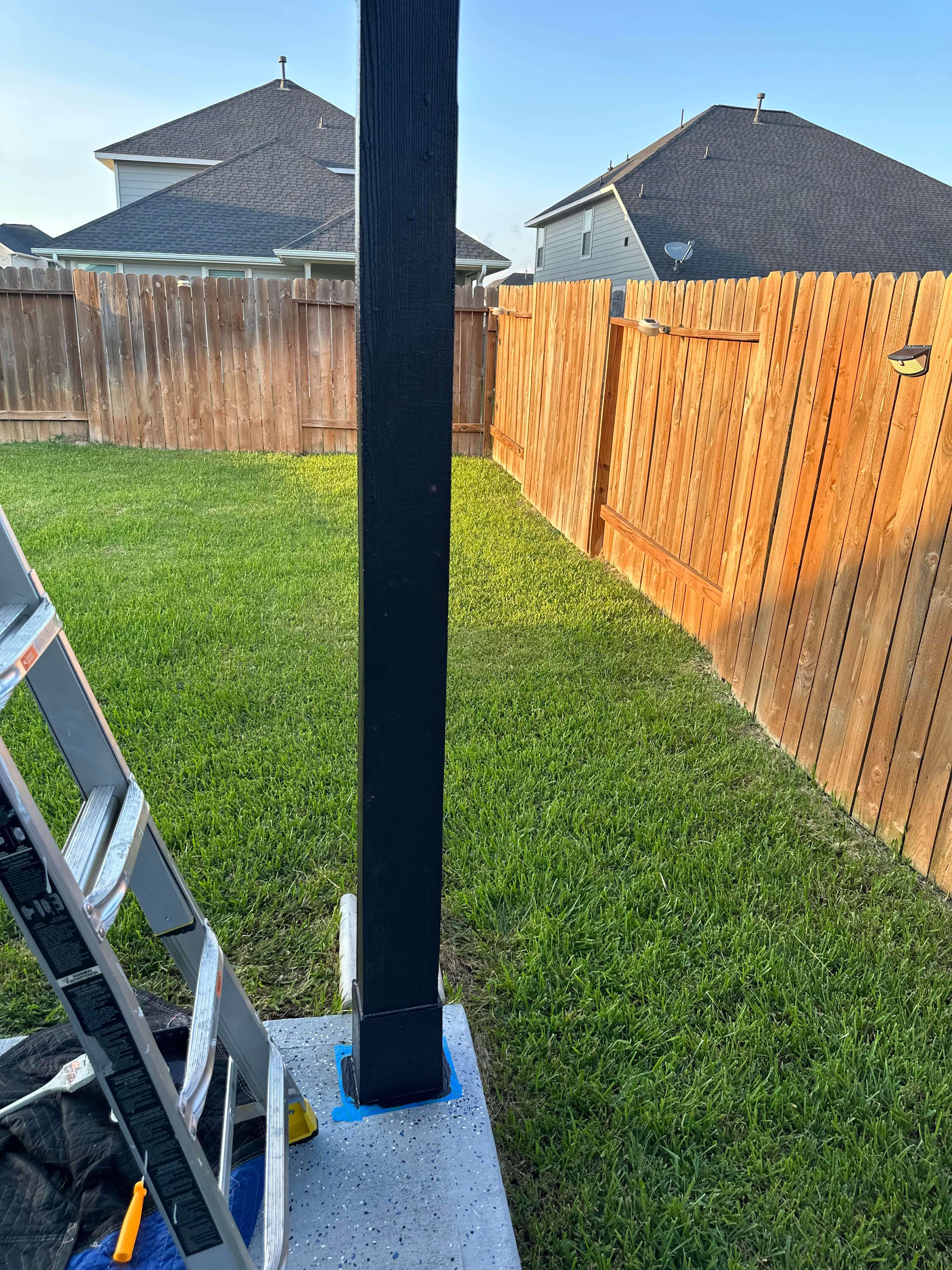 A ladder sitting in the grass next to a wooden fence